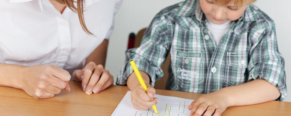 Boy drawing while adult watches encouragingly